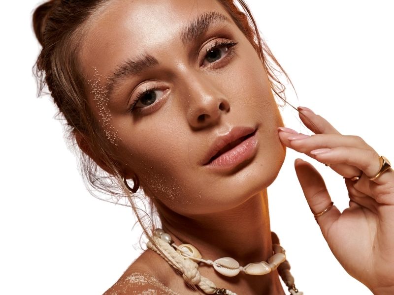 A woman with radiant, tanned skin wears a puka shell necklace.