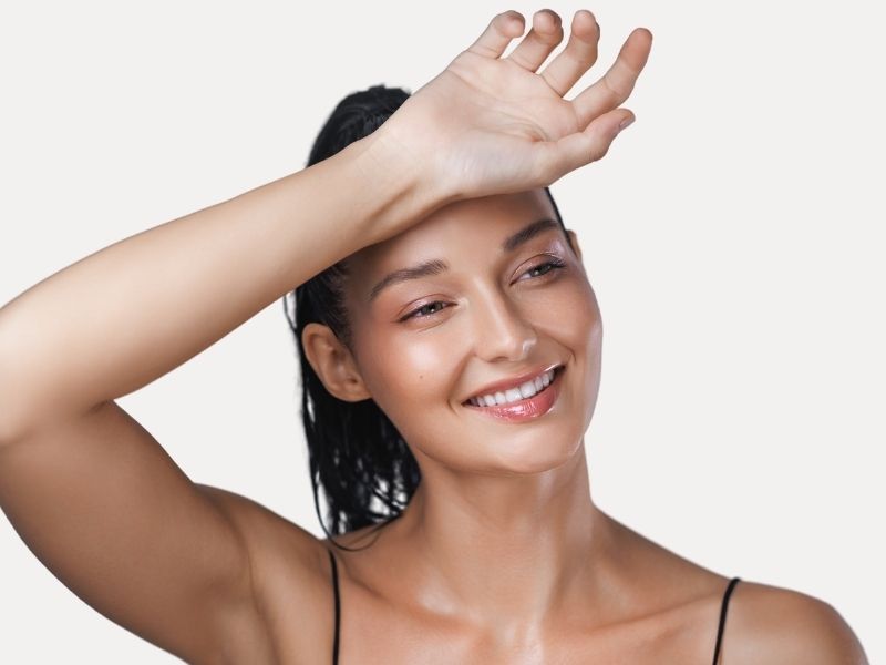 A woman smiles as she places the back of her wrist on her forehead.
