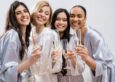 Four women in a bridal party smile and hold champagne glasses.