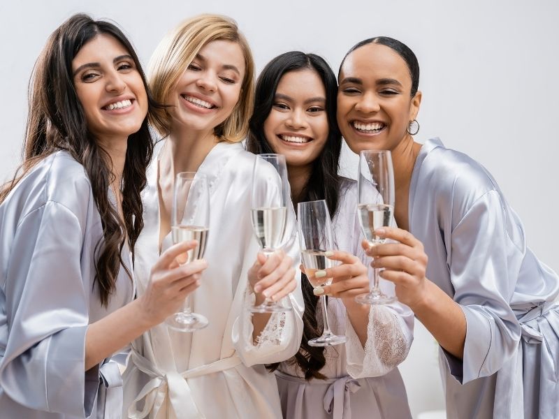 Four women in a bridal party smile and hold champagne glasses.