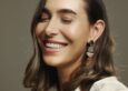 A woman with chandelier earrings smiles into the camera. She has a glowing tan.