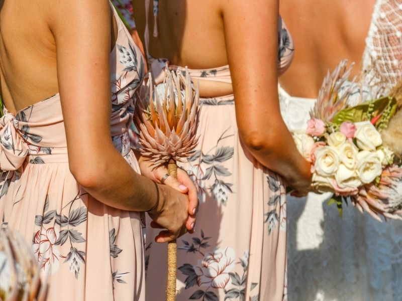 Bridesmaids stand at the altar in a row, holding flowers and sporting glowing tans.